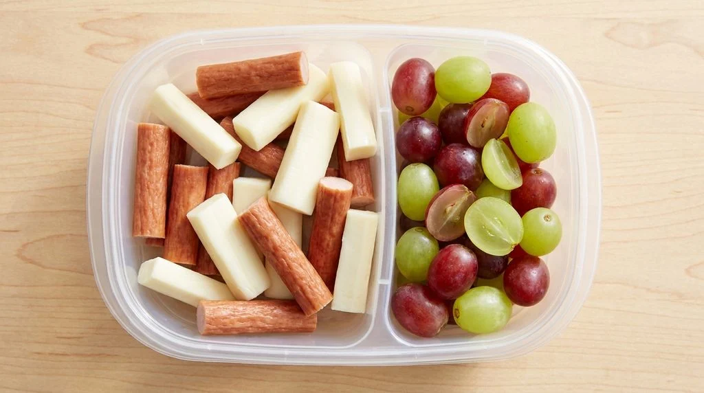 A snack container with turkey sticks, string cheese and grapes for kids