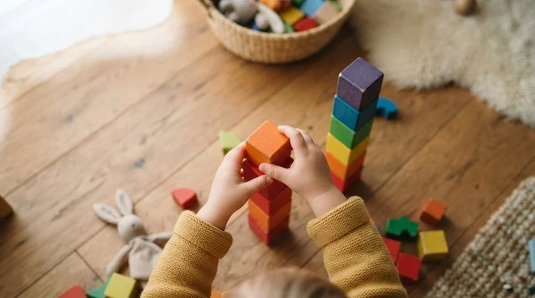 Toddler stacking colourful blocks into a rainbow tower during indoor play