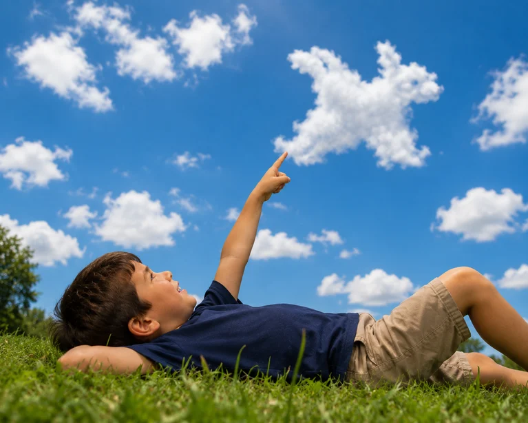Child lying on grass looking for shapes in the clouds.