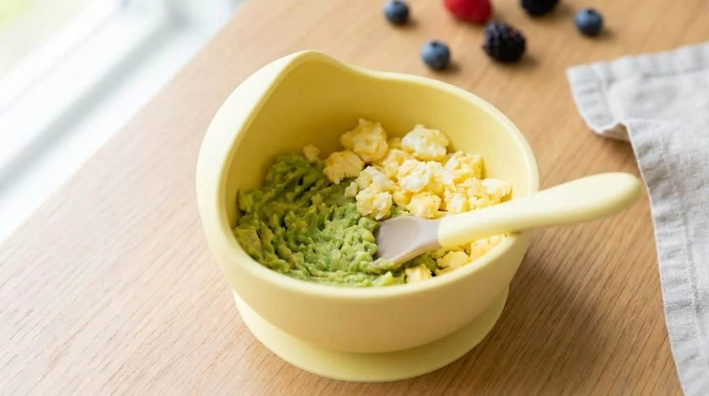 Baby breakfast bowl with mashed avocado and scrambled egg.