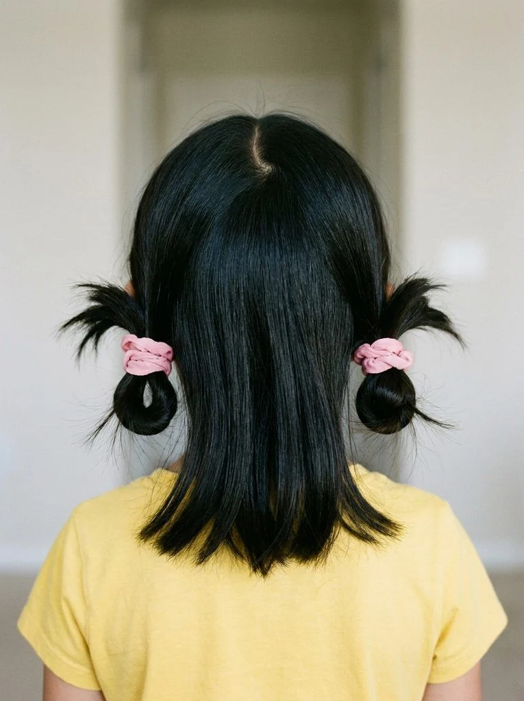 Two low loop buns with matching pink scrunchies and a center part.