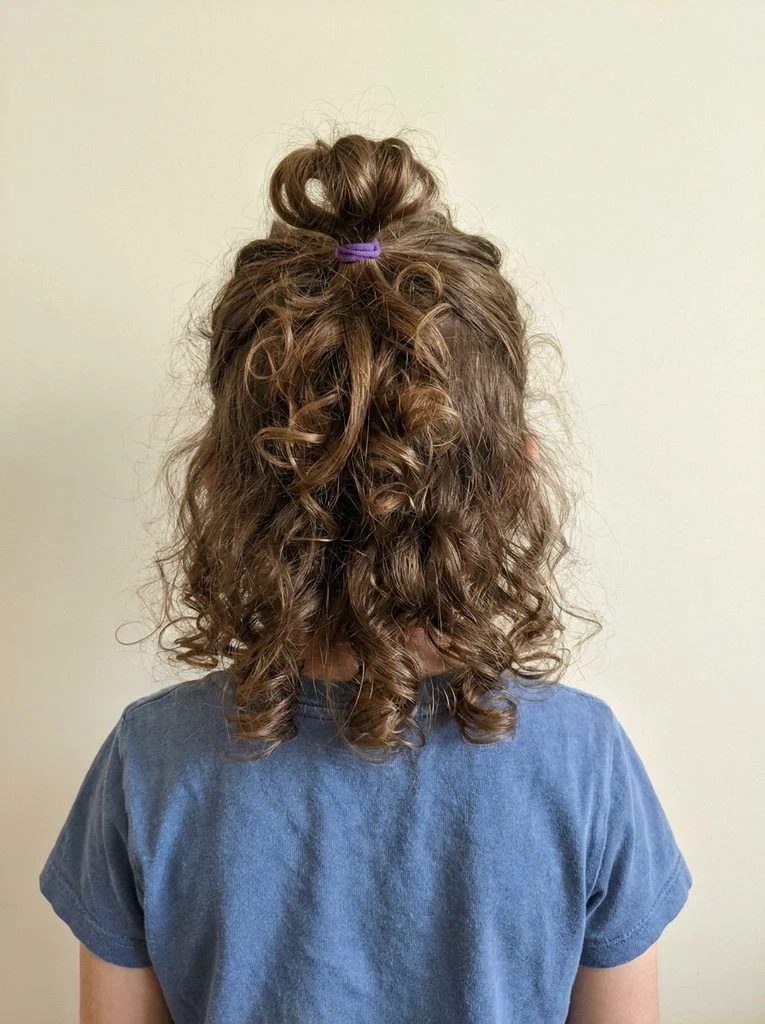 Small half-up loop bun above loose shoulder-length curls.