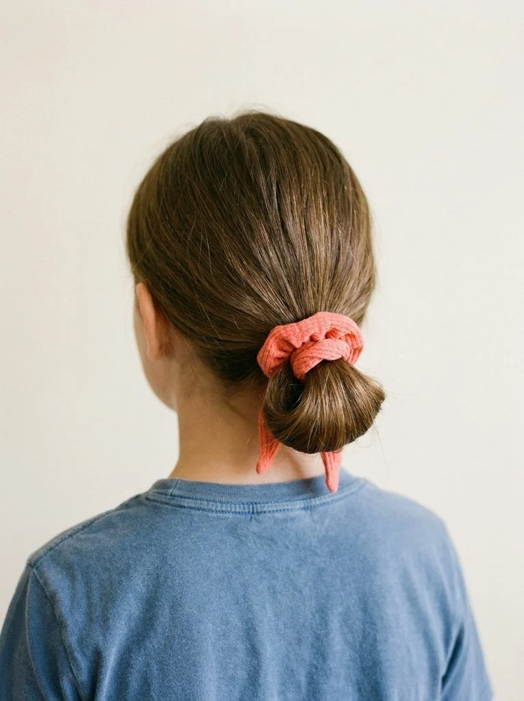 Low loop bun held by a coral scrunchie with loose ends underneath.