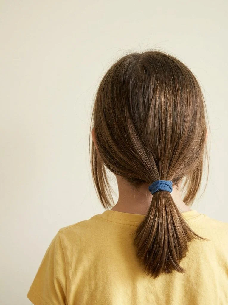 Low ponytail secured at the nape with a blue fabric hair tie.