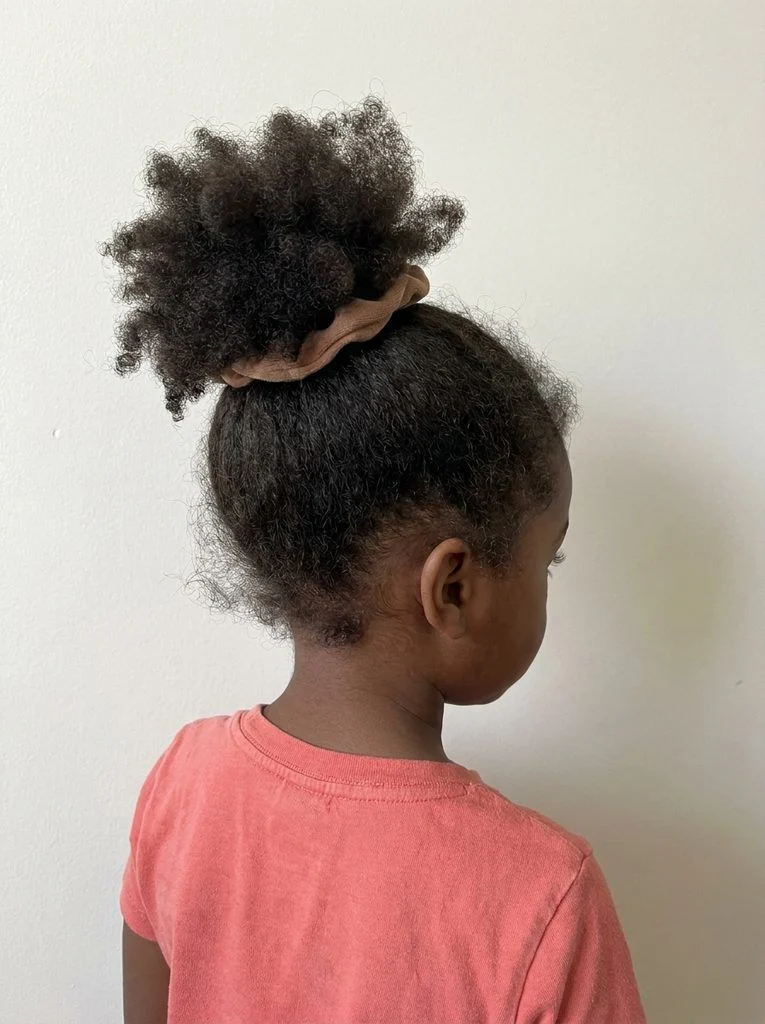 Loose high puff on natural coily hair with softly arranged edges.