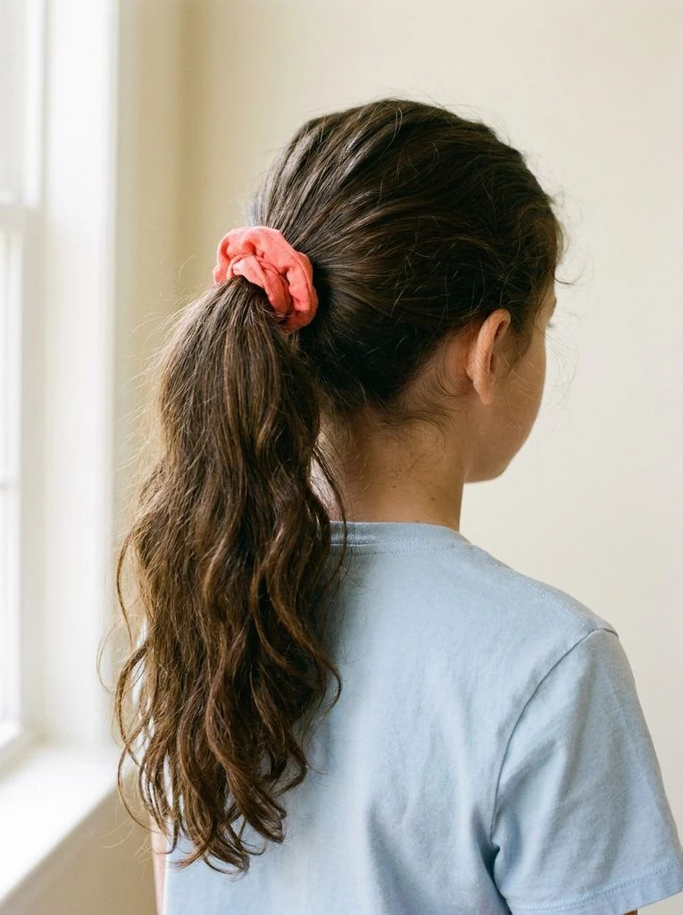 High ponytail on long wavy hair with a coral scrunchie.