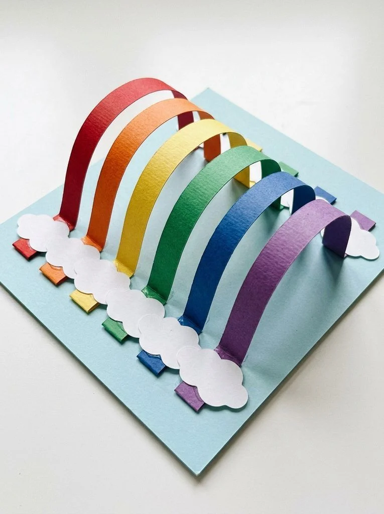 Side-by-side colored paper arches forming a bridge between two paper clouds.